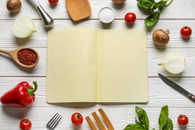 Boş tarif defteri, çatal bıçak takımı ve beyaz ahşap arka plandaki malzemelerden yapılmış çerçeve