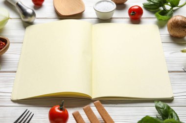 Boş tarif defteri, çatal bıçak takımı ve beyaz ahşap arka plandaki malzemelerden yapılmış çerçeve