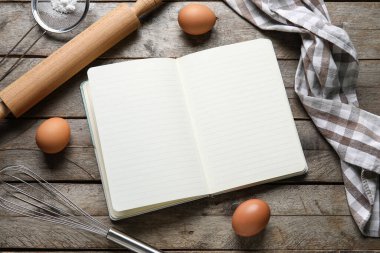 Ahşap zemin üzerinde boş tarif defteri, yumurta ve kap kacak içeren kompozisyon