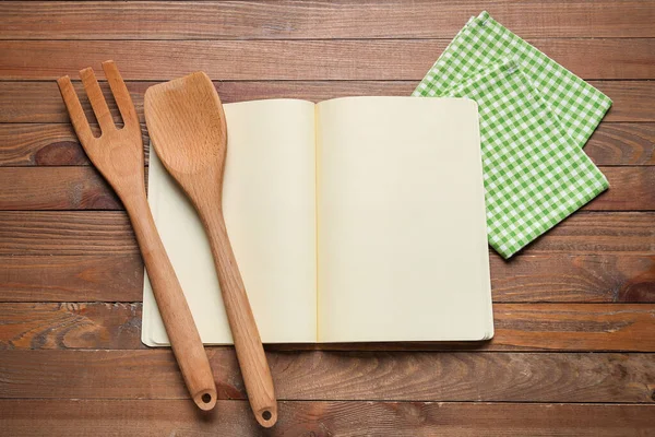 Boş tarif defteri, peçete ve ahşap arka planda ahşap çatal bıçak takımı.
