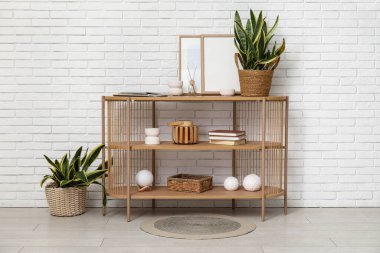 Sansevieria bitkileri, fotoğraf çerçeveleri ve beyaz tuğla duvarın yanında kitapları olan raf ünitesi.