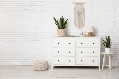 Çekmeceler, tabure ve sansevieria bitkileri odanın içindeki beyaz tuğla duvarın yanında.