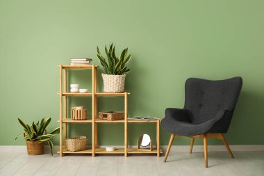 Yeşil duvarın yanında sansevieria bitkileri, koltuk ve raf ünitesi olan şık bir oda.