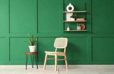 Yeşil duvarın yanında sandalye ve masa olan modern stil bir oda.