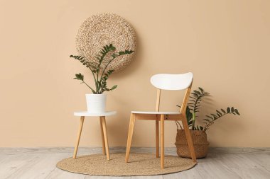 Bej duvarın yanında sandalye, masa ve ev bitkileriyle modern tarz bir oda.