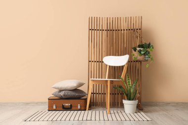 Sandalyesi, katlanmış ekranı ve bej duvarın yanındaki bavulu olan modern tarz bir oda.