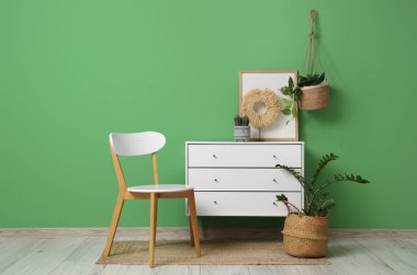 Yeşil duvarın yanında sandıklı ve sandalyeli modern tarz bir oda.