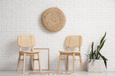 Sandalyeler, bitki örtüsü ve fotoğraf çerçevesi modern odanın içindeki beyaz tuğla duvarın yanında.