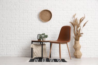 Çimenli vazo, sandalye ve masa modern odanın içindeki beyaz tuğla duvarın yanında.
