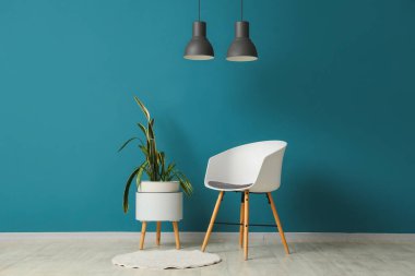 Modern odanın içindeki mavi duvarın yanında sandalye ve bitki var.