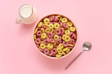 Mısır gevreği halkaları ve pembe arka planda bir sürahi süt.