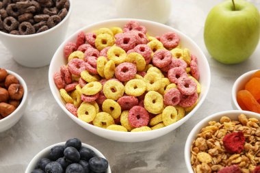 Renkli mısır gevreği halkaları ve gri grunge arka planda malzemeleri olan kaseler, yakın plan.