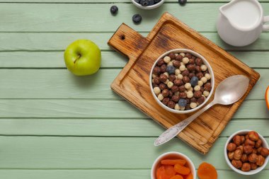 Bir kase çikolatalı mısır topu ve yeşil ahşap arka planda malzemelerle kompozisyon.