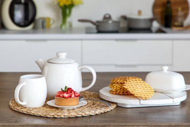 Beyaz çaydanlık, fincan ve lezzetli kek mutfaktaki masada, yakın plan.