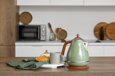 Elektrikli yeşil çaydanlık, fincan ve kurabiyeler mutfaktaki masada, yakın plan.