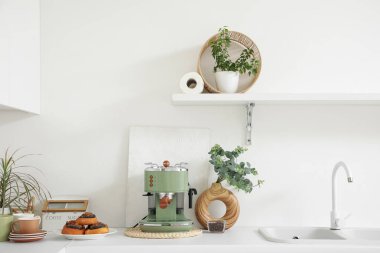 Modern kahve makinesi, tatlı çörekler ve mutfakta okaliptüs dalları olan vazo.