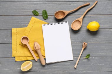 Koyu ahşap arka planda kaşıklar, limonlar ve nane şekerli boş tarif kitabı.