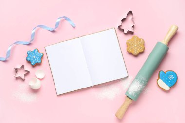 Pembe arka planda merdaneli, kesicili ve Noel kurabiyeli boş tarif kitabı