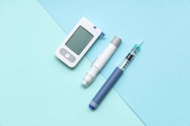 Mavi arkaplanda dijital glukometre ve tükenmez kalemlerle kompozisyon