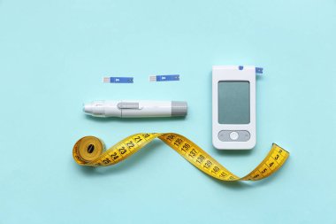 Mavi zemin üzerinde dijital glukometre, test şeritleri, mezura ve tükenmez kalem bileşimi