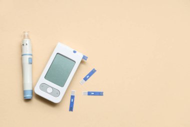 Dijital glukometre, test şeritleri ve bej arkaplan üzerindeki neşter kalem