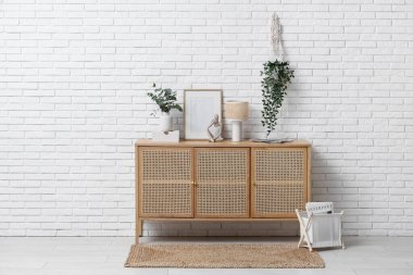 Fotoğraf çerçevesi, lamba ve vazo. Okaliptüs dalları, beyaz tuğla duvarın yanındaki çekmecelerde.