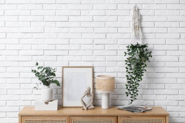 Fotoğraf çerçevesi, lamba ve vazo. Okaliptüs dalları, beyaz tuğla duvarın yanındaki çekmecelerde.