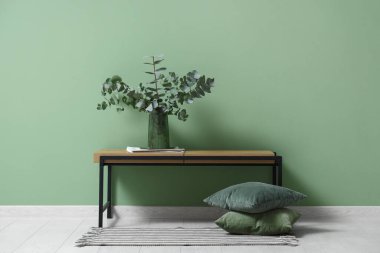 Vase with eucalyptus twigs on bench near green wall in room