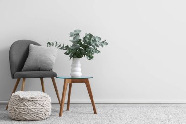 Chair and vase with eucalyptus twigs on table near white wall in room
