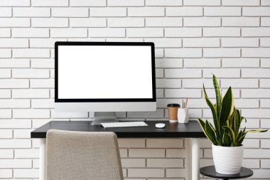 Comfortable workplace with modern computer on table near white brick wall
