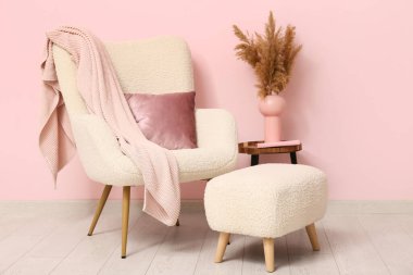 Interior of room with pouf, table and armchair near coral wall