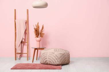 Interior of room with pouf, stepladder and table near coral wall