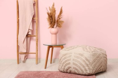 Interior of room with pouf, stepladder and table near coral wall
