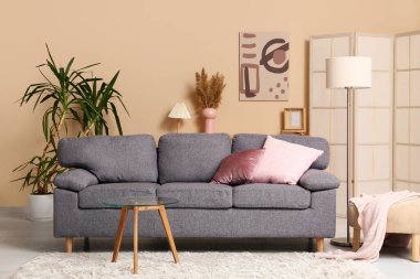 Grey sofa with coral cushions near beige wall in interior of living room