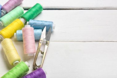 Beyaz ahşap zemin üzerinde makas ile renkli iplik makaraları