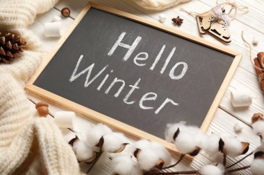 Yazılı tebeşir tahtası Hello Kışları, marşmelovlar, pamuk çiçekler ve beyaz ahşap arka planda süveter