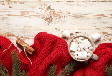 Bir fincan marşmelovlu kakao, köknar dalları ve beyaz ahşap arka planda kazak. Merhaba kış.