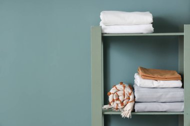 Yeşil duvarın yanında katlanmış yatak çarşafları olan raflar.