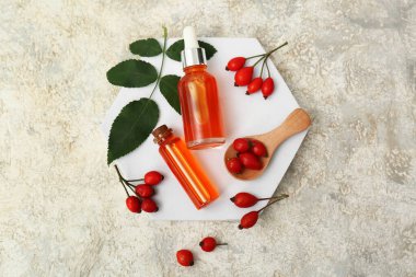 Gri arkaplanda kozmetik gül kalça yağı ve böğürtlen şişeleriyle dekoratif podyum