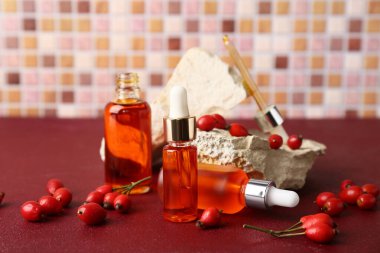 Kırmızı masada böğürtlenli kozmetik gül yağı ve taş şişeleri.