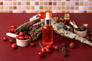 Kozmetik gül, kalça yağı ve böğürtlen dolu ağaç kabuğu kırmızı masada.