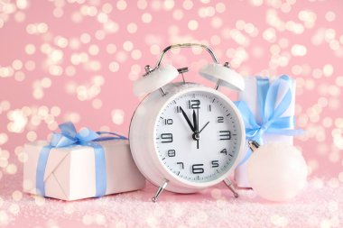 Alarm saati, hediye kutuları ve pembe arka planda Noel balosu.