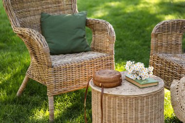 Rahat hasır koltuklar, papatya çiçekleri, kitap ve çanta parkta, açık havada kahve masasında.