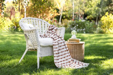 Rahat beyaz hasır koltuk battaniyeli ve kitaplarla parkta, açık havada kahve masasında.