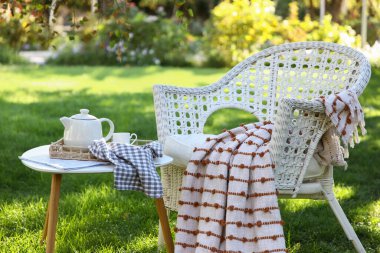 Rahat beyaz hasır koltuk, battaniye, gazete ve çaydanlık parkta, açık havada kahve masasında.