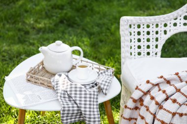 Rahat beyaz hasır koltuk, battaniye, gazete ve çaydanlık parkta, açık havada kahve masasında.