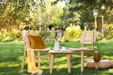 Konforlu hasır sandalyeler, sedir, kahve fincanı ve vazo çiçekleri parkta, açık havada.