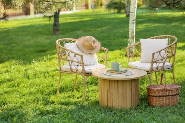 Rahat hasır koltuklar, yastıklar, sepet ve bir fincan kahve parkta, açık havada.