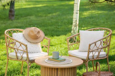 Rahat hasır koltuklar, yastıklar, kitap ve kahve parktaki masada, açık havada.