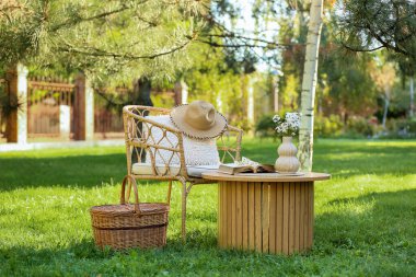 Sepeti, kitabı ve vazosu olan rahat bir hasır koltuk. Parktaki kahve masasında, açık havada.